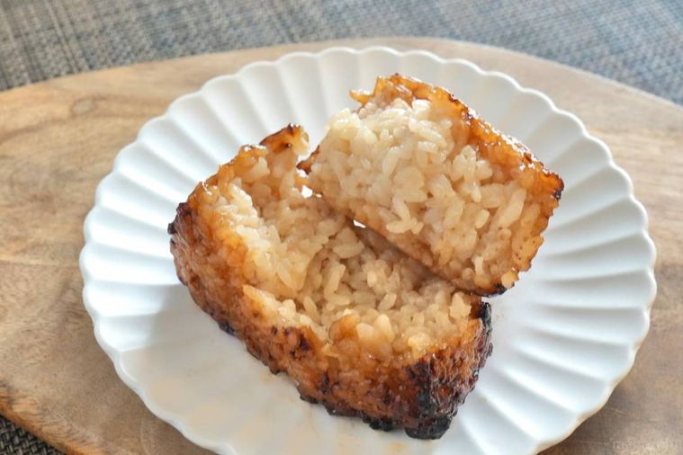 木のカッティングボードと白い皿にのった冷凍の焼きおにぎりを半分に割った様子