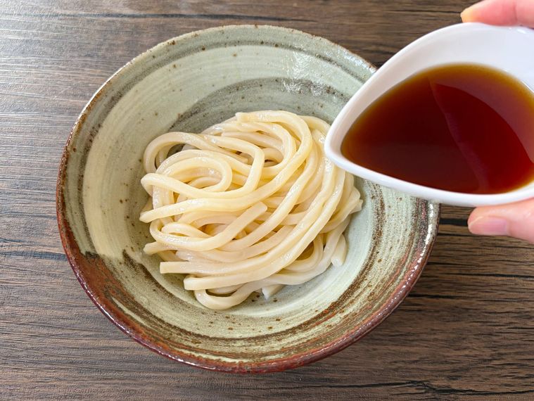 器に入った冷やしたうどんに冷たいつゆを加える様子