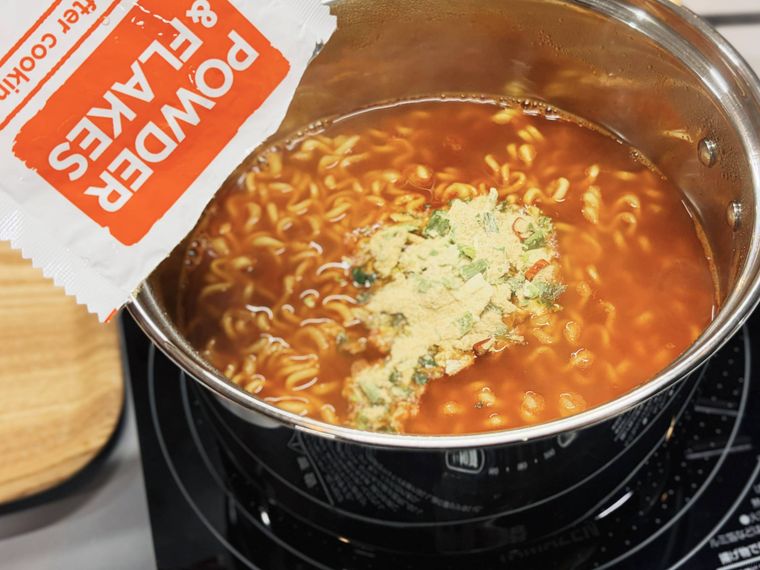 麺の入ったスープにかやくを入れる様子