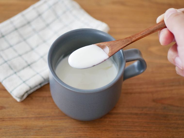 ダークグレーのマグカップに入ったホットヨーグルトを木製のスプーンですくう様子