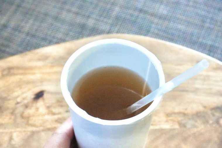 木のカッティングボードにのった飲むおだしのカップ飲料にストローを刺した様子