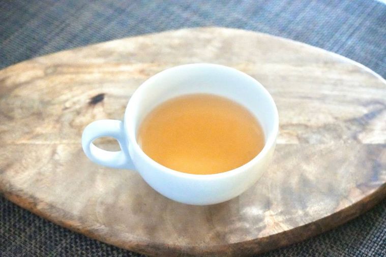 木のカッティングボードにのった飲むおだし入りの白いカップ