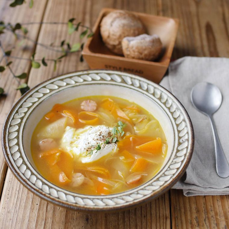 縁取りのある皿に盛りつけられた野菜とポーチドエッグのスープ