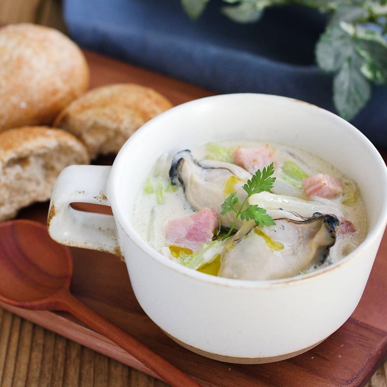 白いカップに入っている牡蠣と白菜の豆乳スープ、パンなど