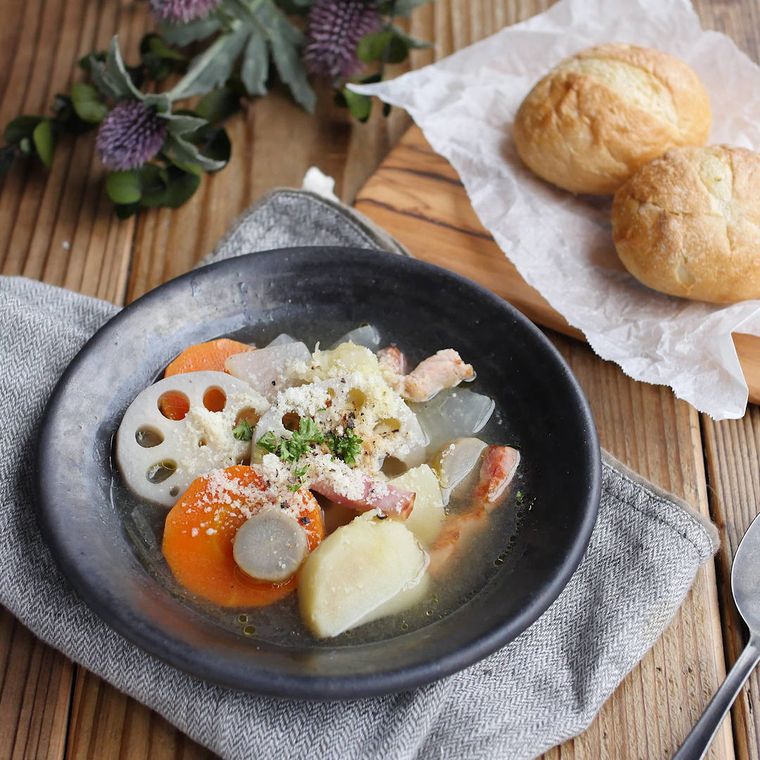 黒い皿に盛りつけられた大根やれんこん、にんじんのコンソメスープ