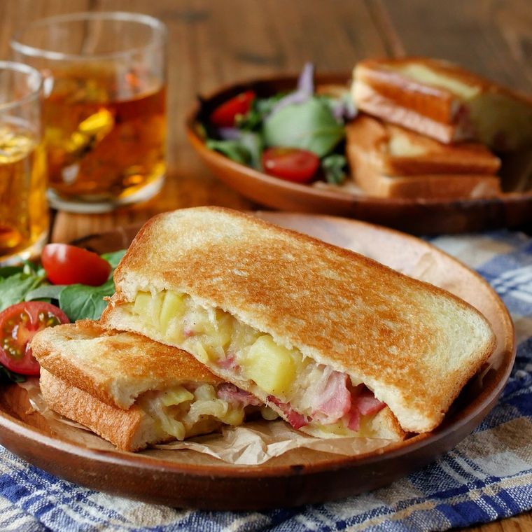 木の皿に盛りつけられたベーコンポテトホットサンドにビールが添えられている