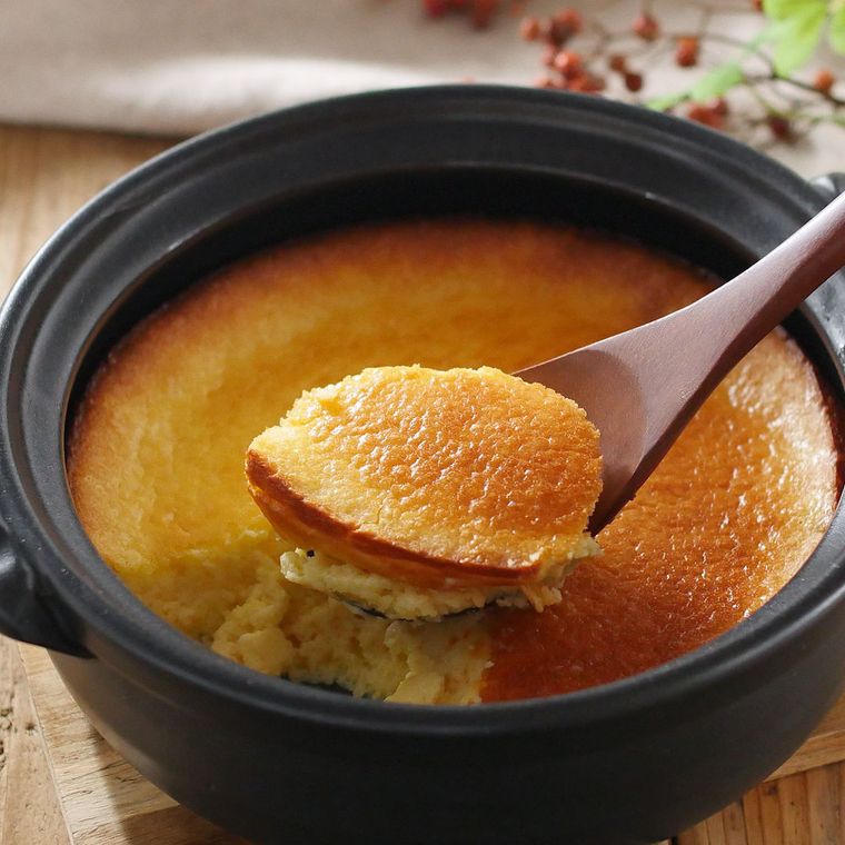 黒い土鍋に入っているチーズケーキを木のスプーンですくった様子