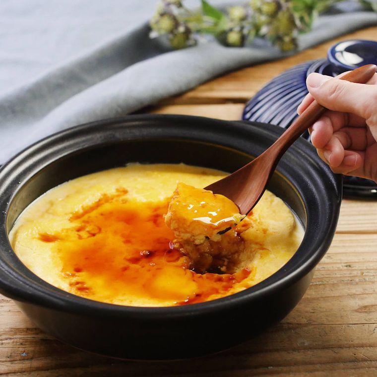 土鍋に入っているプリンとカラメルを木のスプーンですくった様子