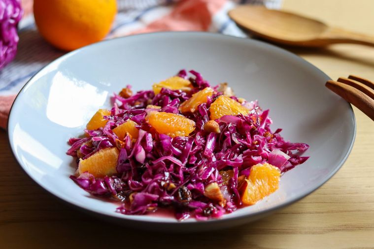 白い皿に紫キャベツとオレンジ皿の奥に木のスプーンや丸ごとオレンジ