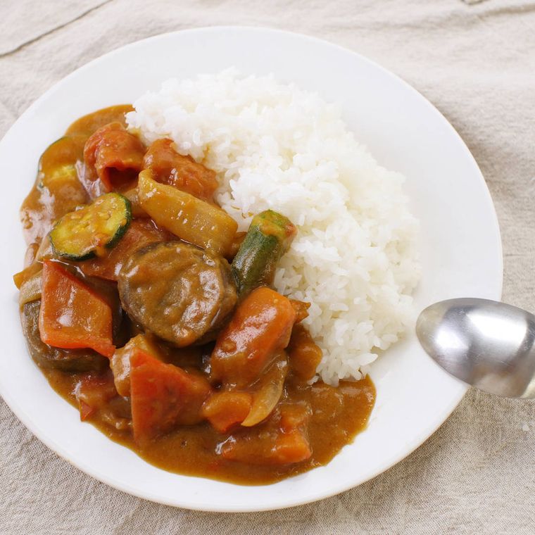 白い皿に入った玉ねぎ、なす、ズッキーニなどの野菜カレー