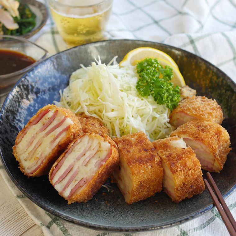 黒っぽい皿に盛り付けられているベーコンとマッシュポテトのカツ
