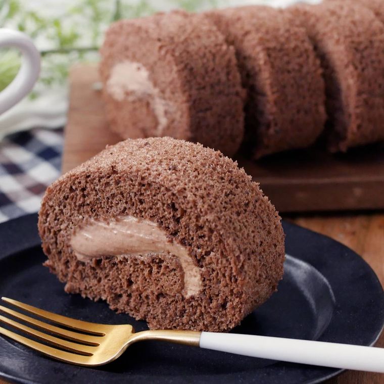 黒い皿に盛りつけられたココアロールケーキにフォークが添えられている