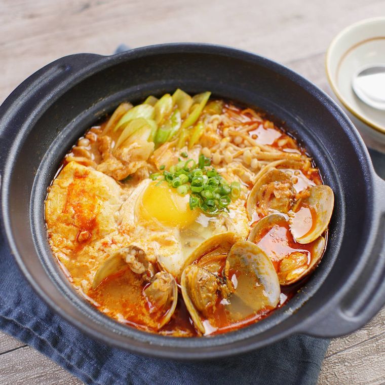 黒い土鍋に入っているあさりや豚バラ肉、長ねぎの韓国風湯豆腐