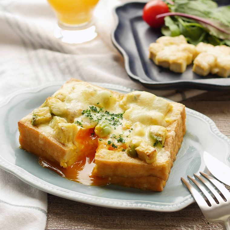 薄いブルーの皿にアボカドと厚揚げのチーズ焼きが盛られ、フォークとナイフが添えられている様子