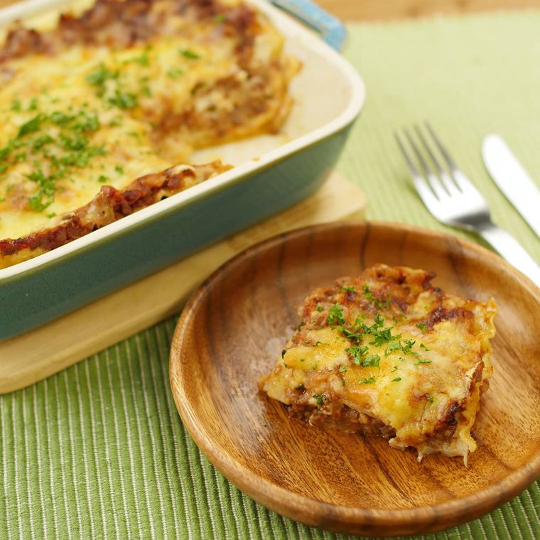 青緑色の容器から木製の皿に取り分けられたミートソースとチーズのラザニア