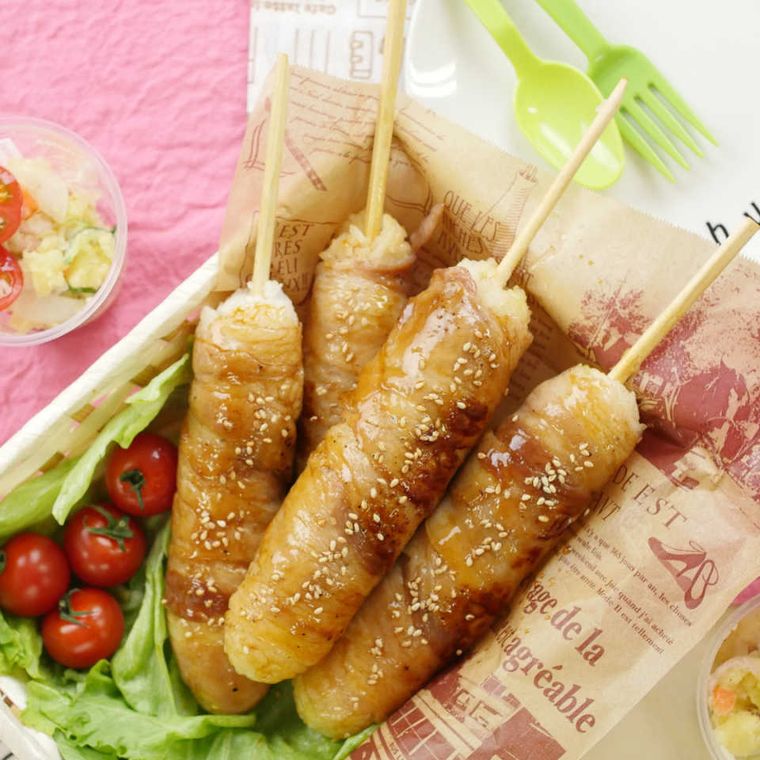 棒に刺さっている肉巻きおにぎりがお弁当箱の中に4本入っている