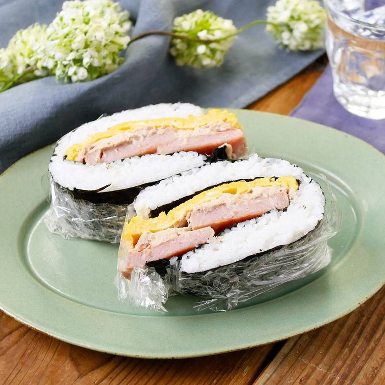 緑色のお皿の上にラップにまかれているツナマヨポークたまごおにぎらずが2つ盛られている