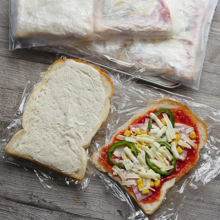 ラップの上にあるホワイトソースを塗った食パンとピザの具材をのせた食パン
