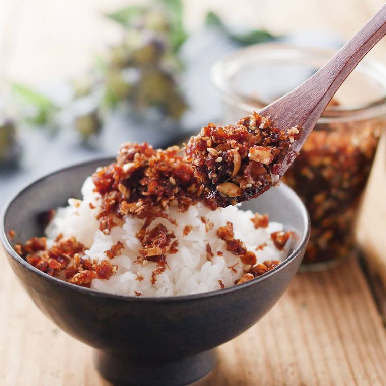 黒いお茶碗によそったご飯に、木のスプーンで食べるしょうゆをのせている様子