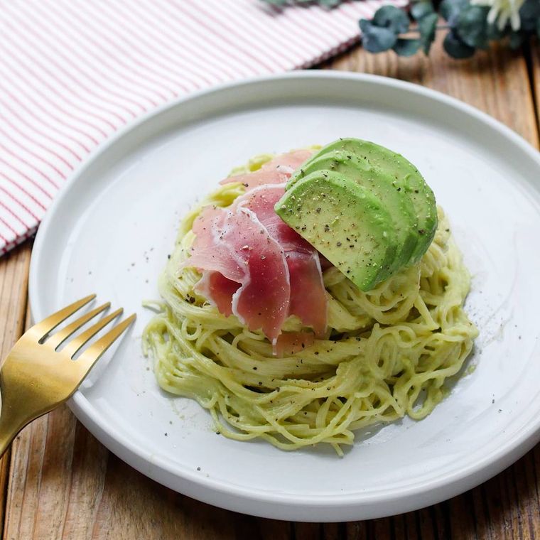 白い丸皿に盛り付けられたアボカドと生ハムのパスタ