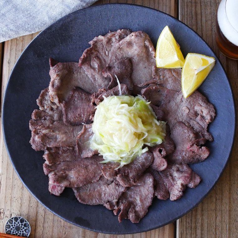 ねぎ塩だれが中央におかれたさっぱり牛タンステーキが黒い円形の皿に盛り付けられているところ
