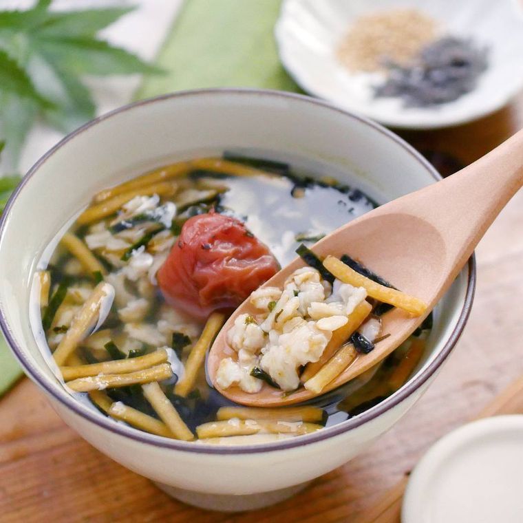 白いボウルに入って、梅干しが添えられたオートミールお茶漬けを木のスプーンですくっている様子