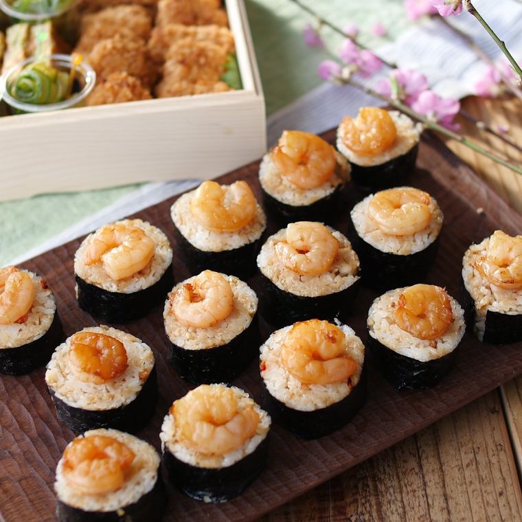 木のプレートに盛りつけられている揚げ玉入りえびのせ海苔巻き