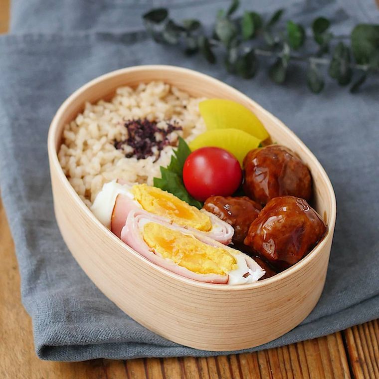木製の弁当箱に簡単ハムエッグやごはん、ミートボールなどが盛られている様子
