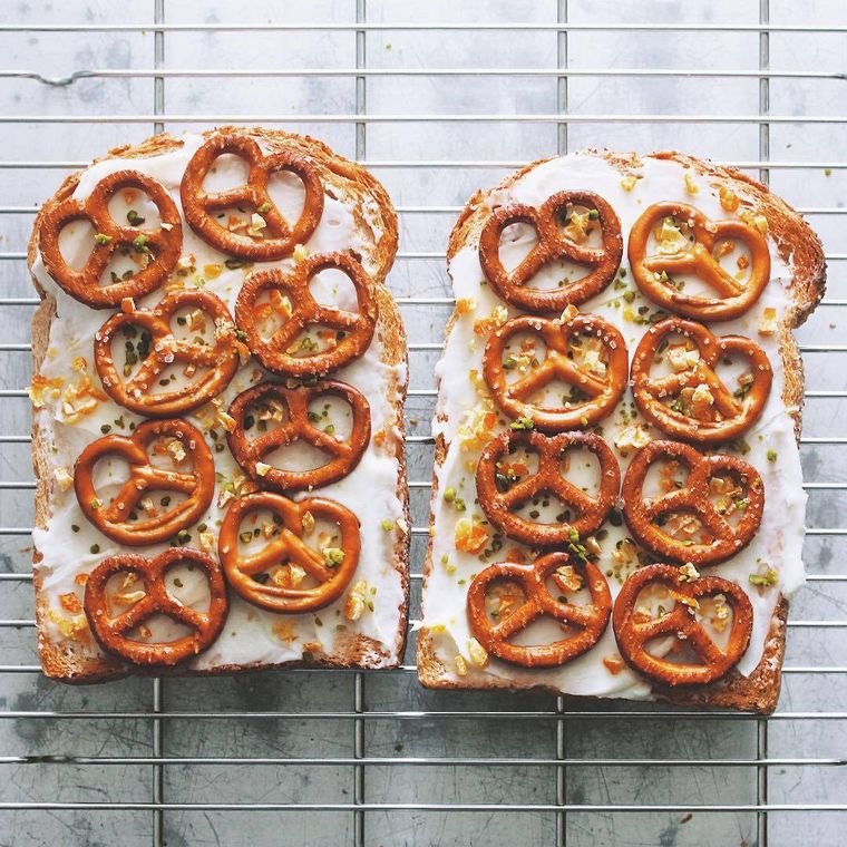 ケーキクーラーの上に並べられた、クリームチーズ、プレッツェル、オレンジピール、ナッツをトッピングしたトースト