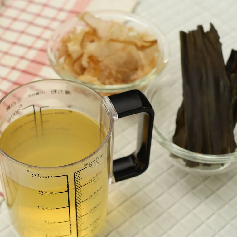 計量カップに入っただし汁と器に入ったかつおぶしと昆布