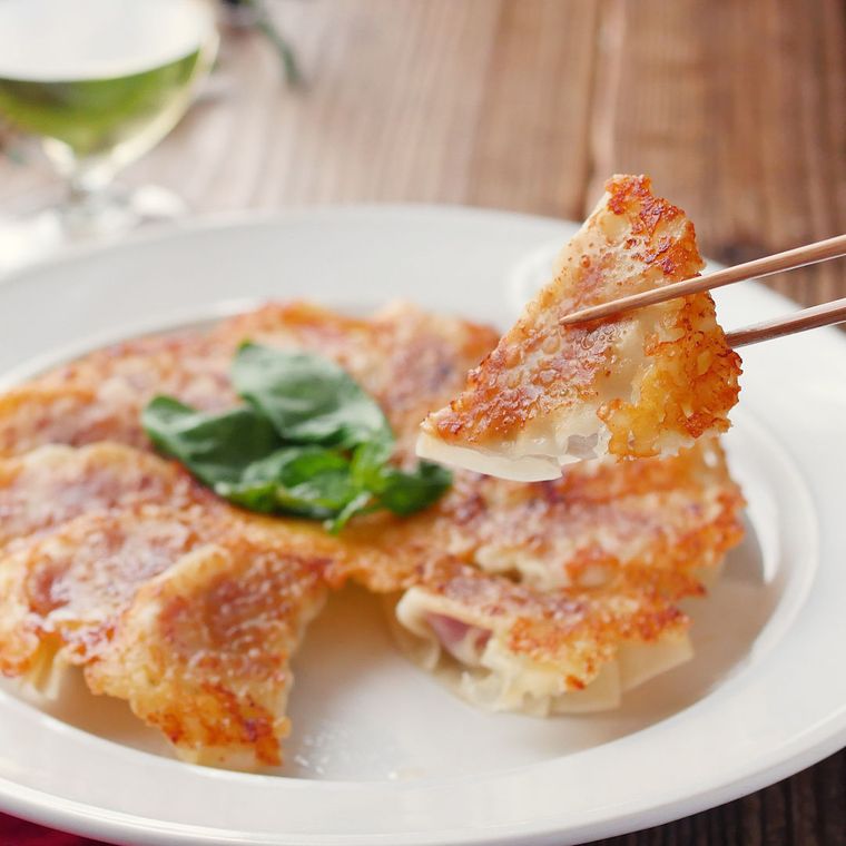 白い皿に盛りつけられたイタリアン餃子を箸でつまんでいる様子