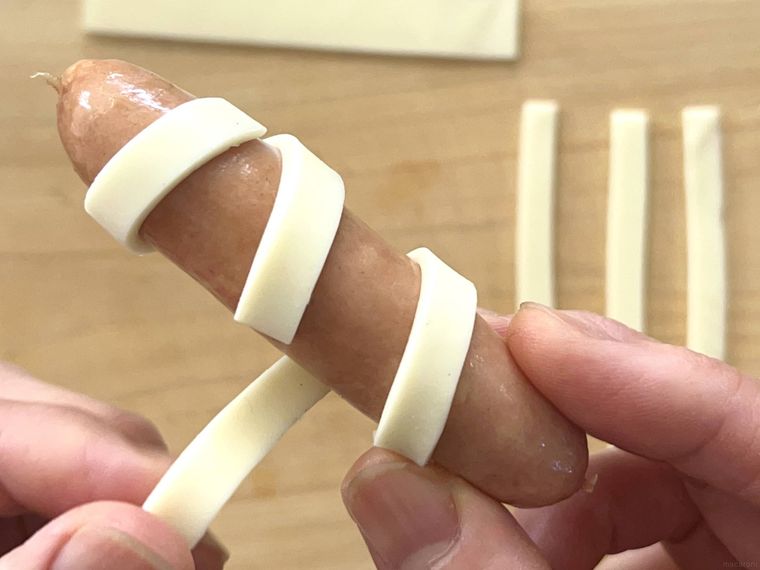 ウインナーに細く切ったスライスチーズを巻き付けているところ