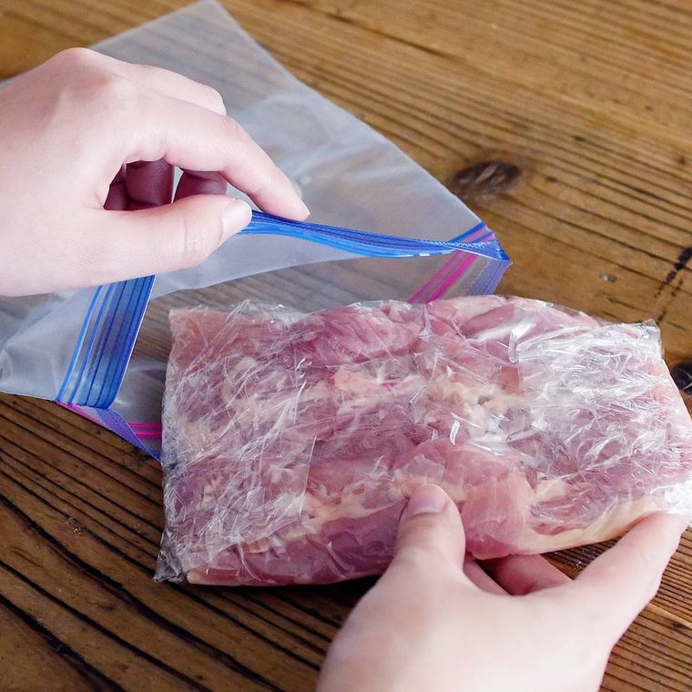 鶏もも肉をラップに包み、フリーザーバッグに入れている様子