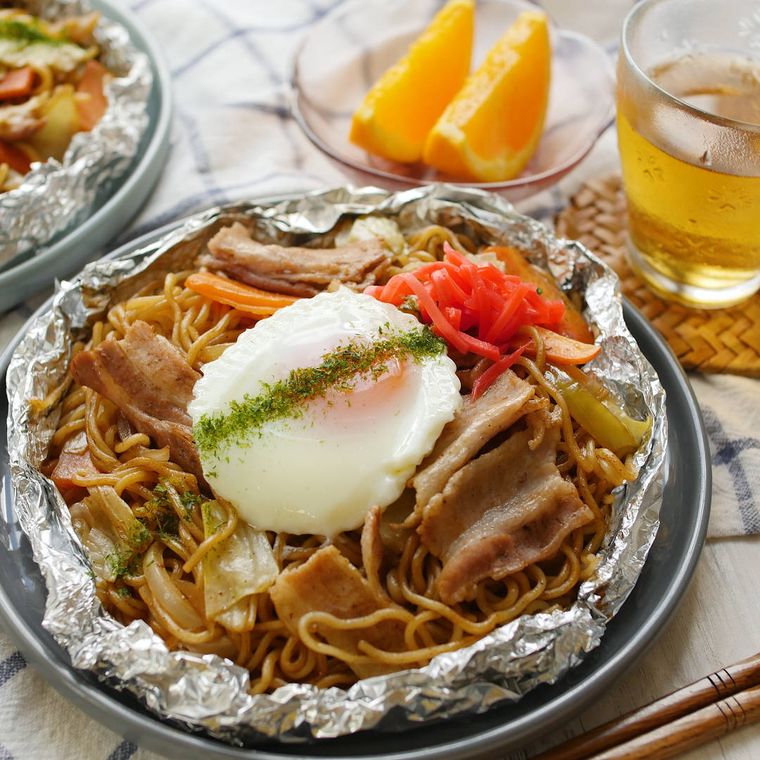 焚き火で調理したアルミホイル焼きそばがホイルの中で野菜や豚肉とともに香ばしく焼かれて盛り付けられているところ