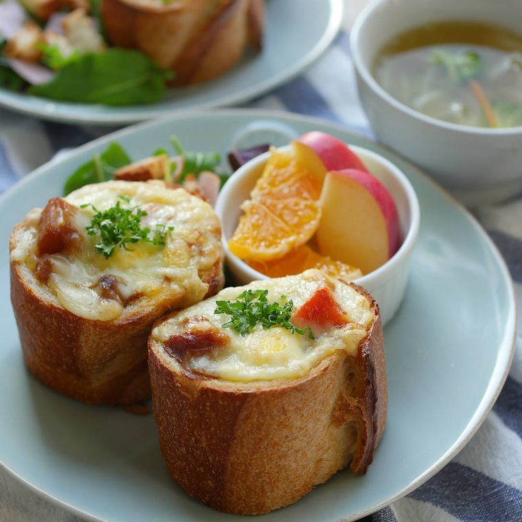 焚き火で焼いたお月見カレーパングラタンがチーズがとろけた状態で青い円形の皿に盛り付けられているところ