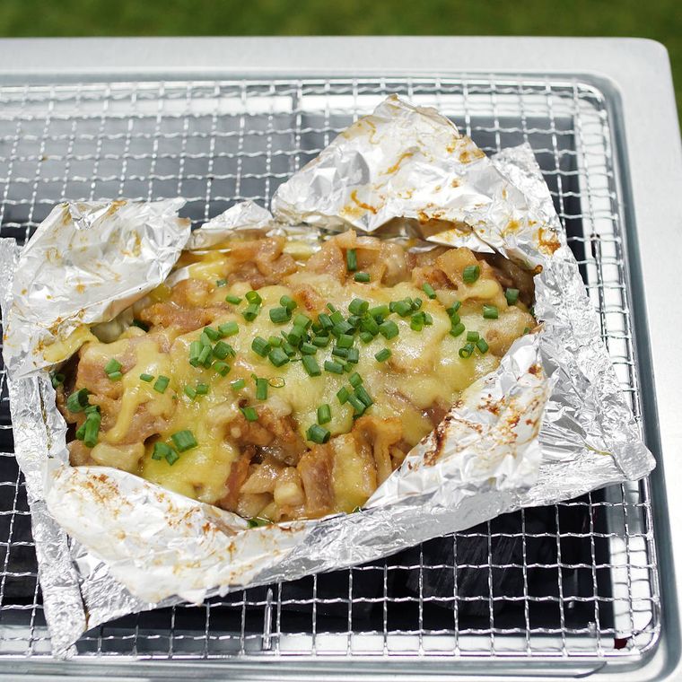 焚き火で調理した豚みそキャベツのホイル焼きがアルミホイルに包まれ、網の上で焼かれているところ