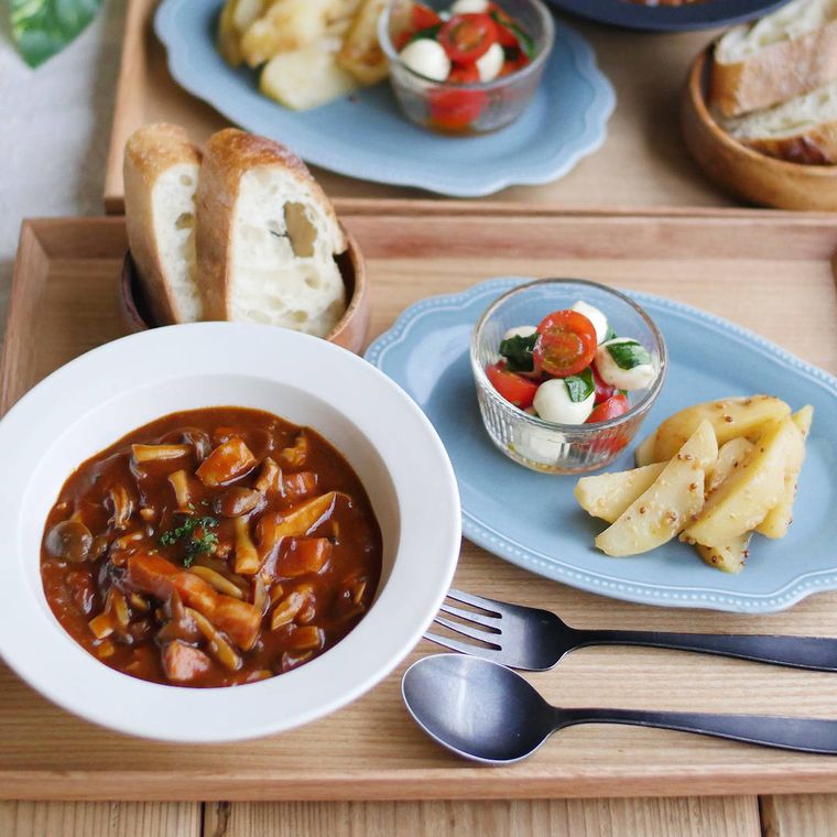 木製のトレーの上に並べられたシチューやパン、サラダ