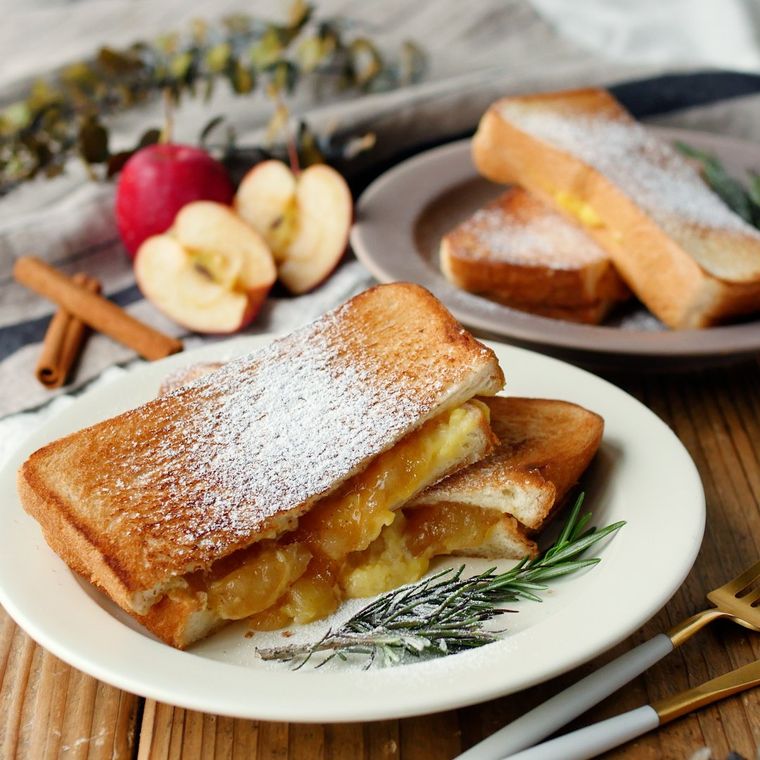 白い皿に盛られた、半分にカットされたカスタード入りりんごホットサンド