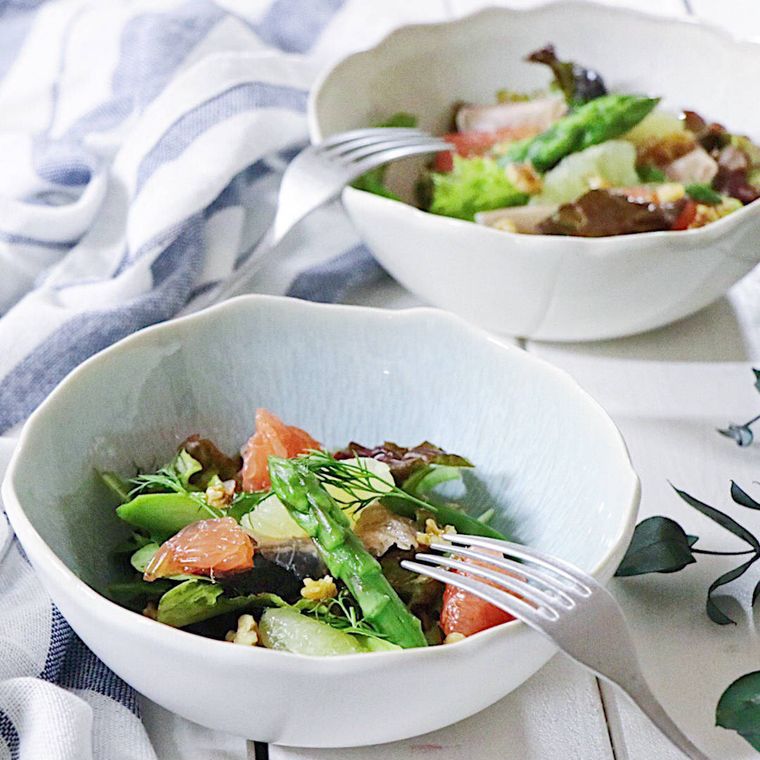 アスパラとグレープフルーツのサラダが入った白いボウルに、銀フォークがかけられている様子