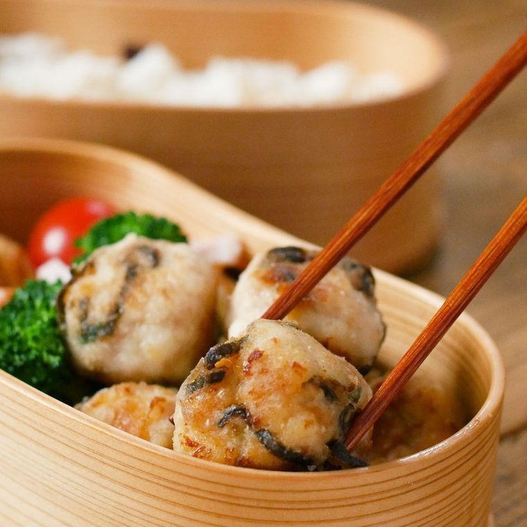 わっぱの弁当箱に入った塩こんぶつくねを、箸で持ち上げる様子