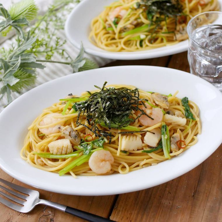 三つ葉と魚介の和風ペペロンチーノが白い皿に盛り付けられているところ