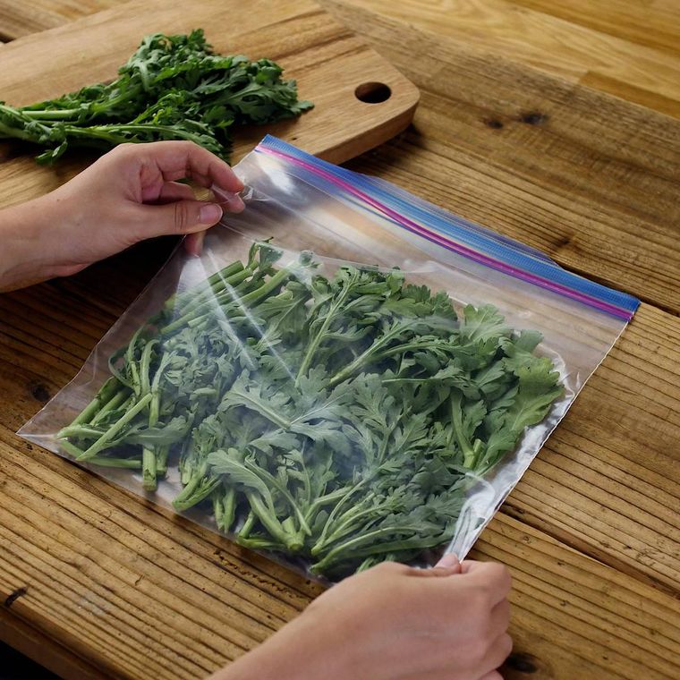 木製のテーブルの上で春菊を保存袋に入れている手