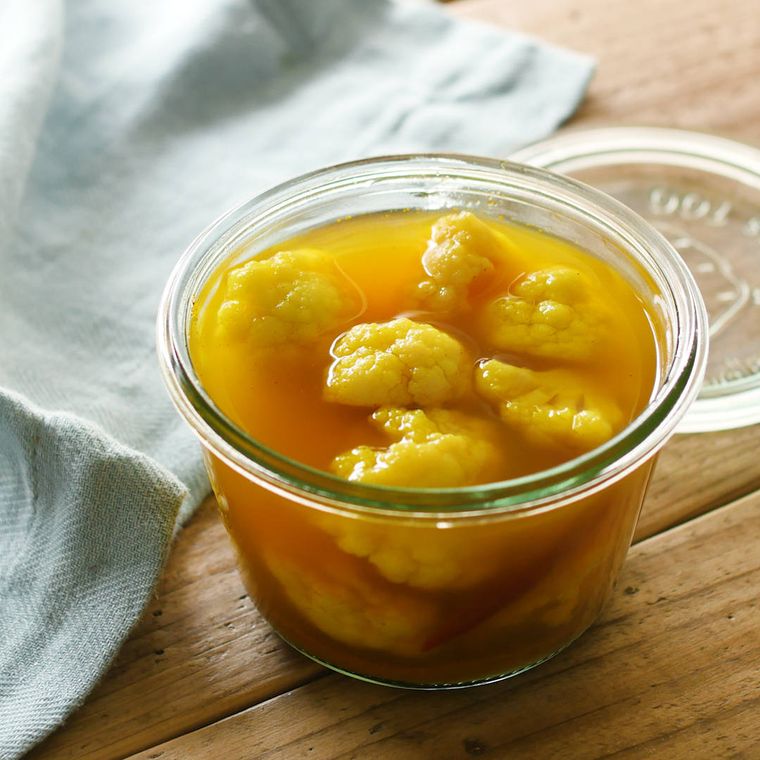 透明なガラスの保存容器に入れられたカレーピクルスが、木の机の上に置かれている