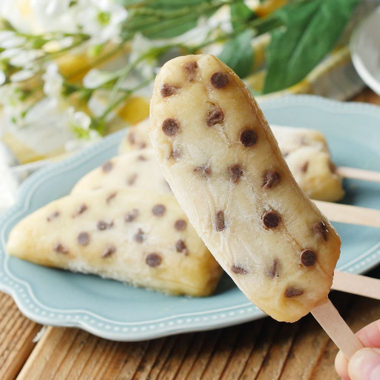 水色の皿に並んだチョコバナナアイスキャンディーを、1本持っている様子