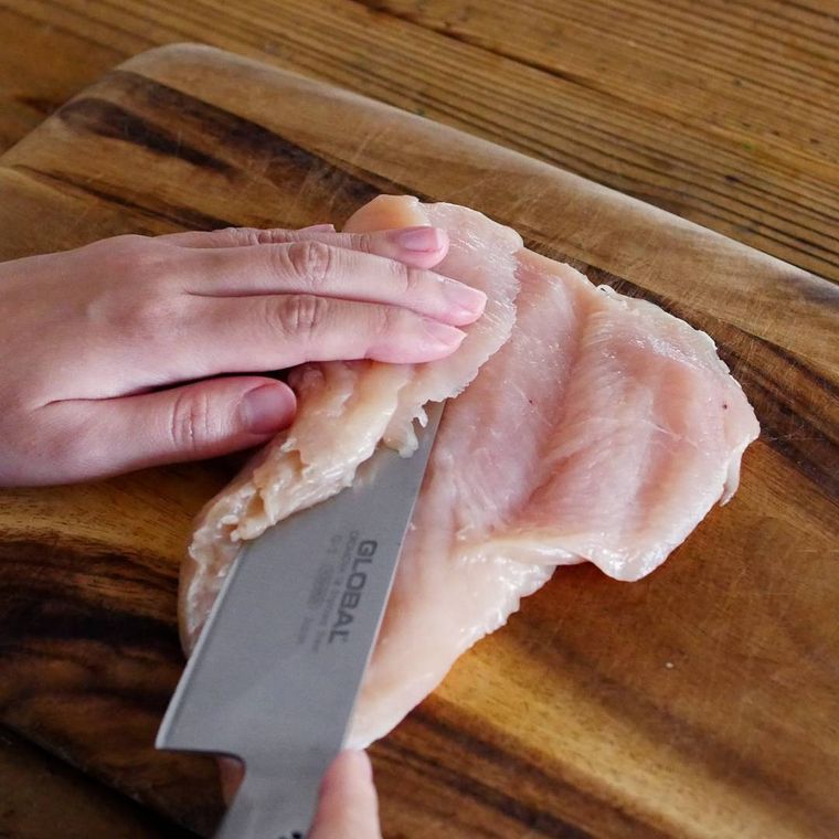 木製のカッティングボードの上で、鶏むね肉の厚さが均等になるよう、切れ目を入れて開いている様子