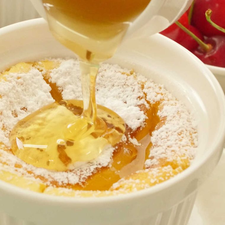 白いココットに入ったスフレチーズケーキに、上からはちみつをかける様子