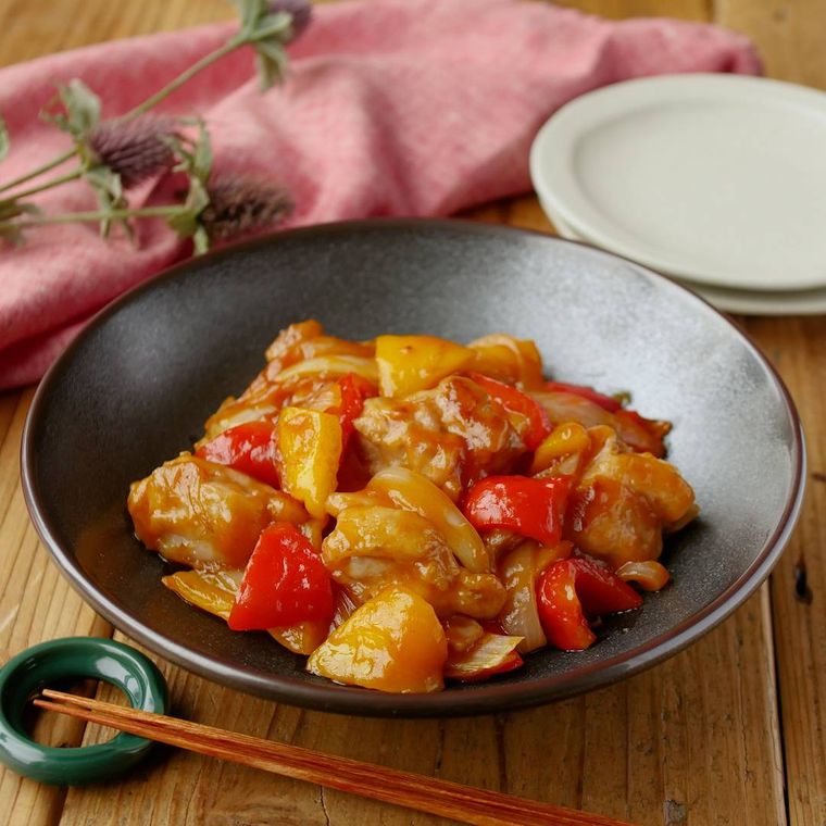 濃色の深皿に盛りつけられている鶏もも肉と2色パプリカの甘酢炒め