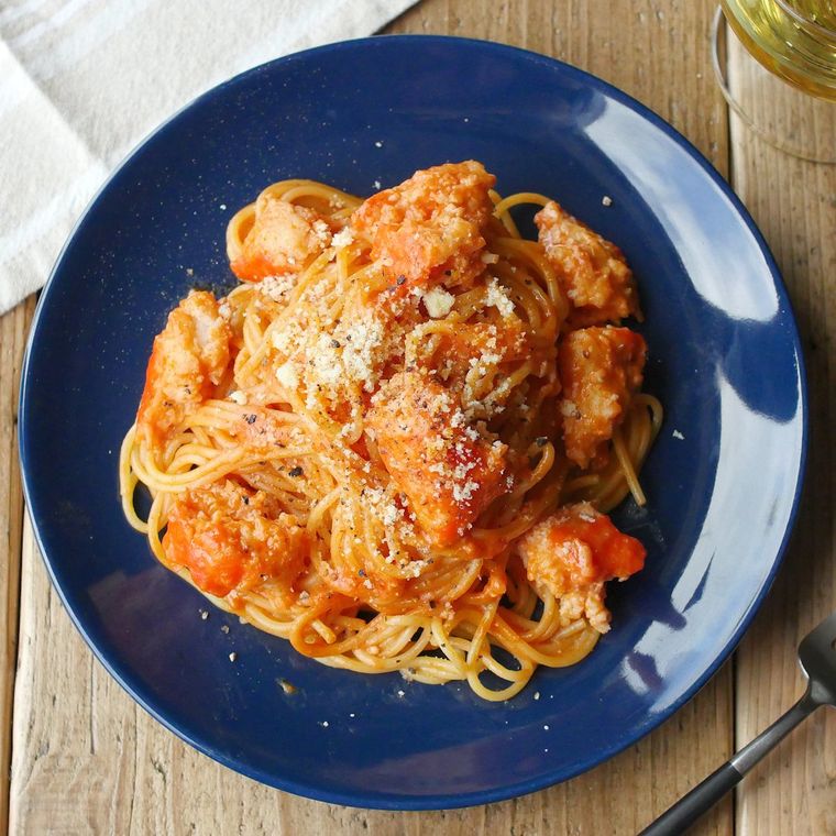 青い皿にカニかまのトマトクリームスパゲティが盛られている様子