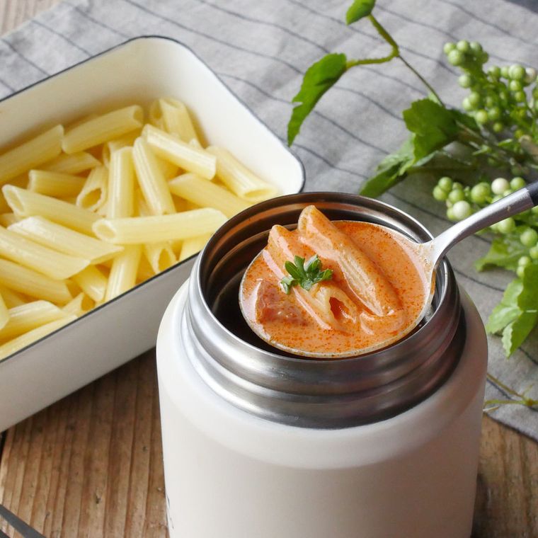 白いスープジャーに入ったトマトクリームペンネをスプーンですくっている様子