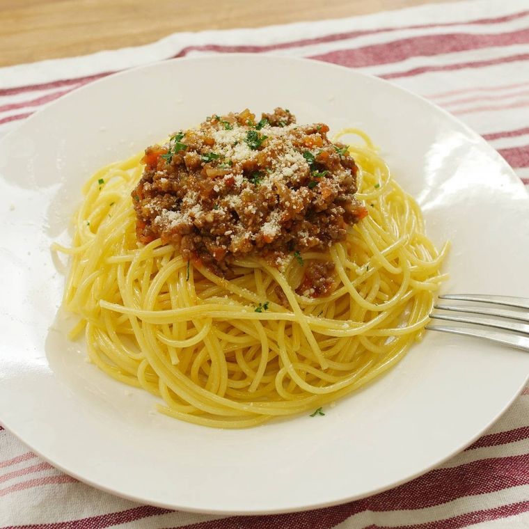 白い器に盛り付けた粉チーズがかかっているミートソーススパゲッティ